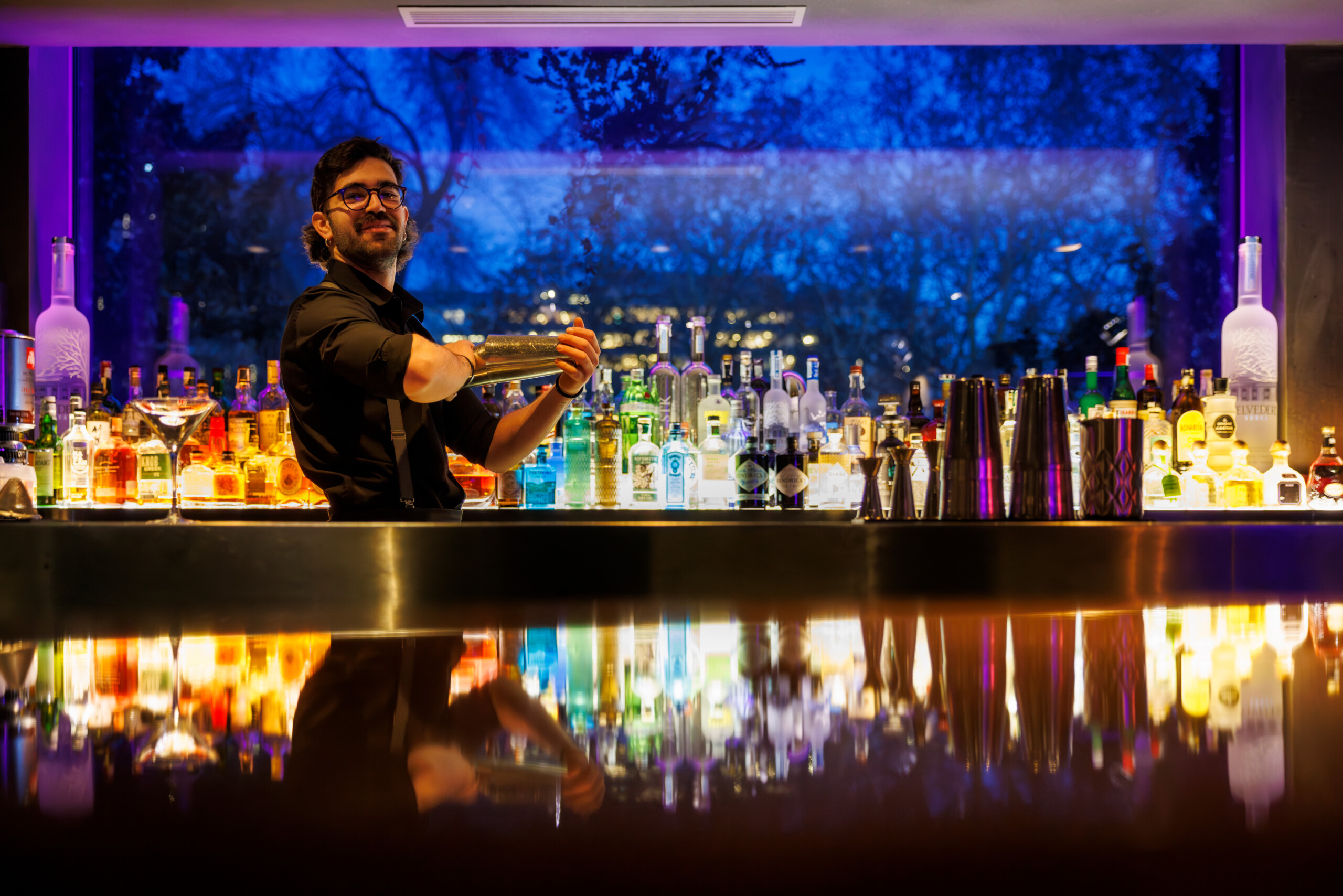 STK bartender making a cocktail at a vibrantly neon blue-lit bar