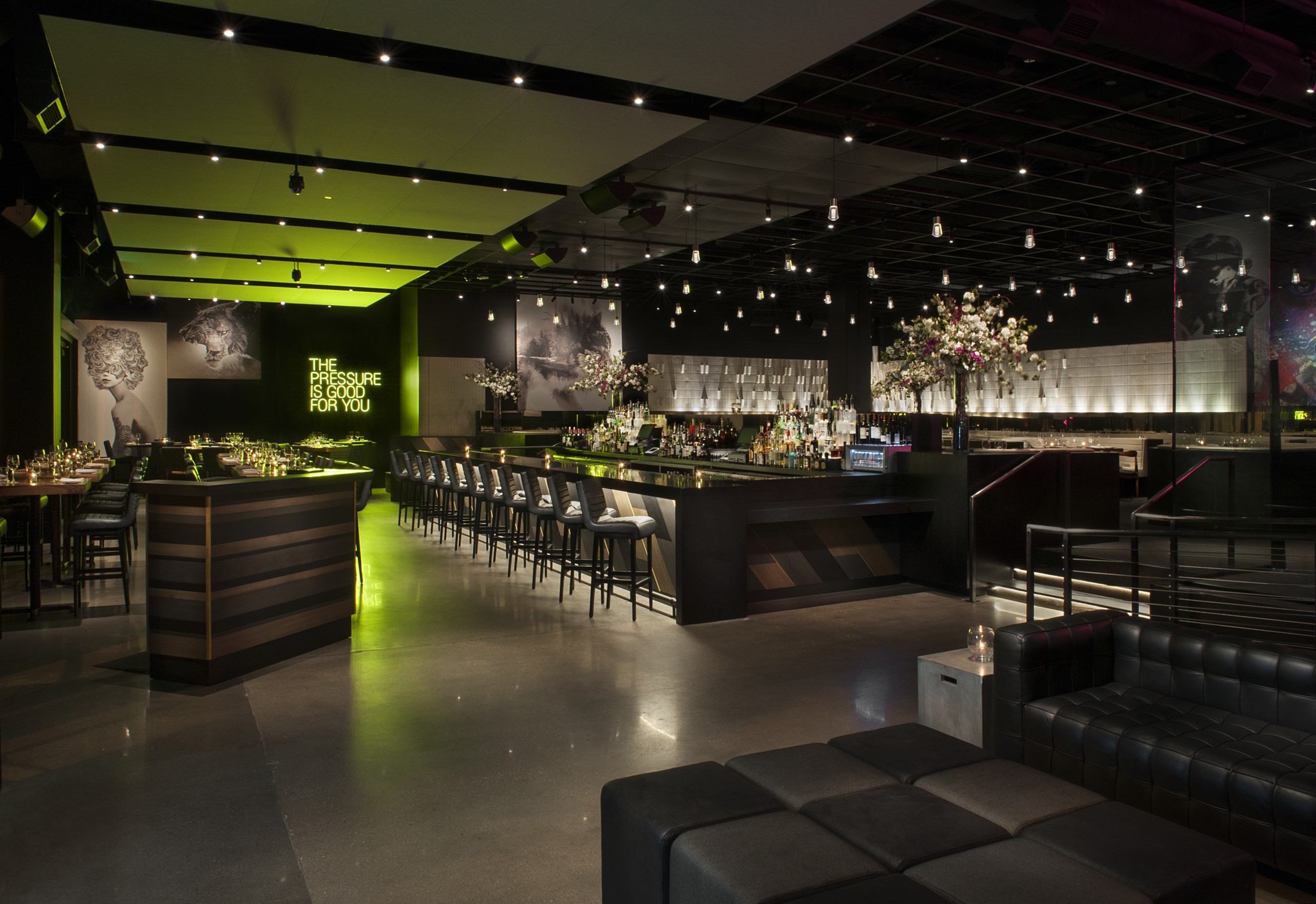 Interior of a Denver restaurant and bar. Green accent lighting highlights the back wall, where a neon sign reads 