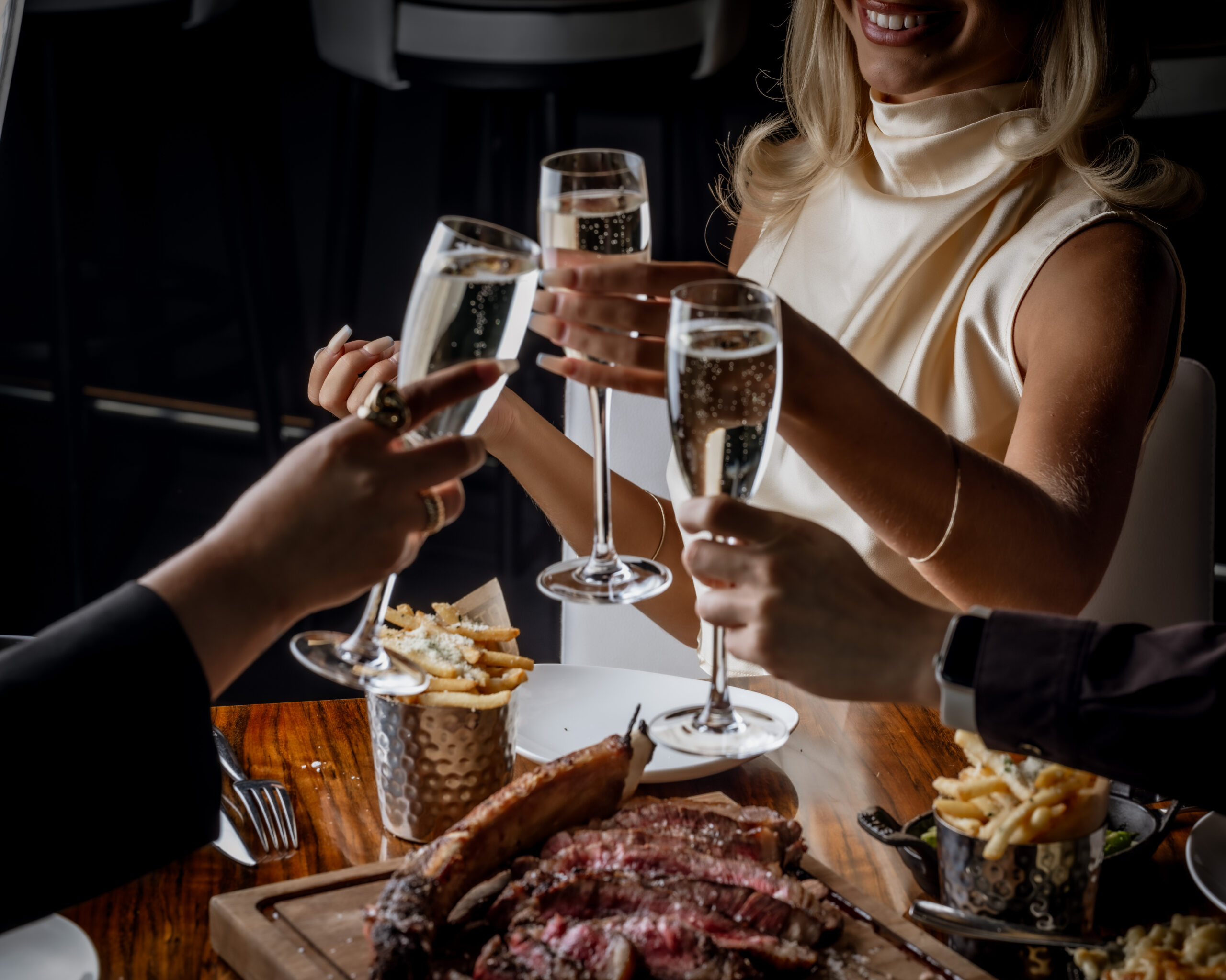 Cheers to STK. Happy diners enjoying a toast of Sparkling White Wine with steak and fries placed on the table