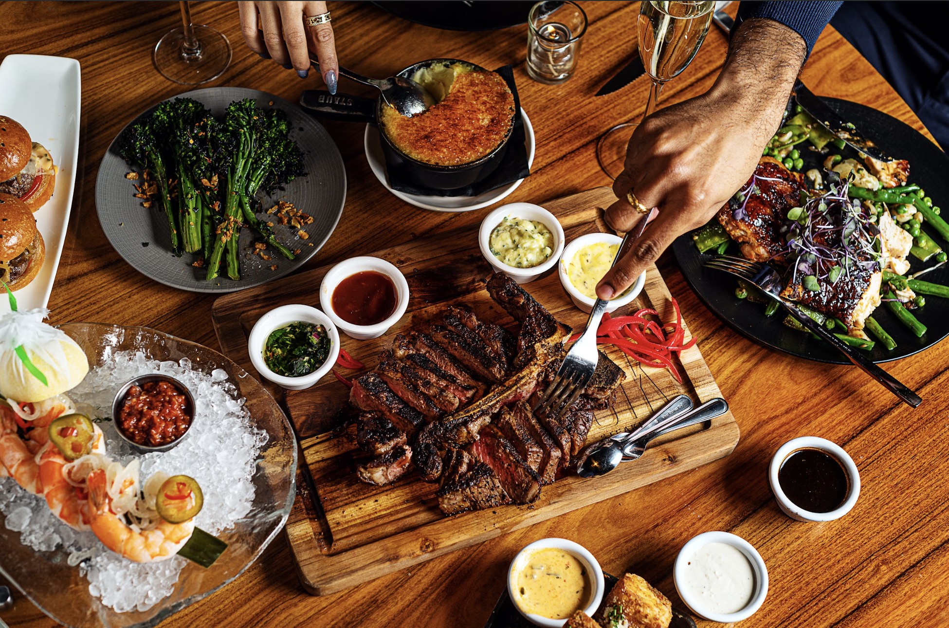 A table laid with delicious food. Including a steak cut into thin slices, prawns and various dips